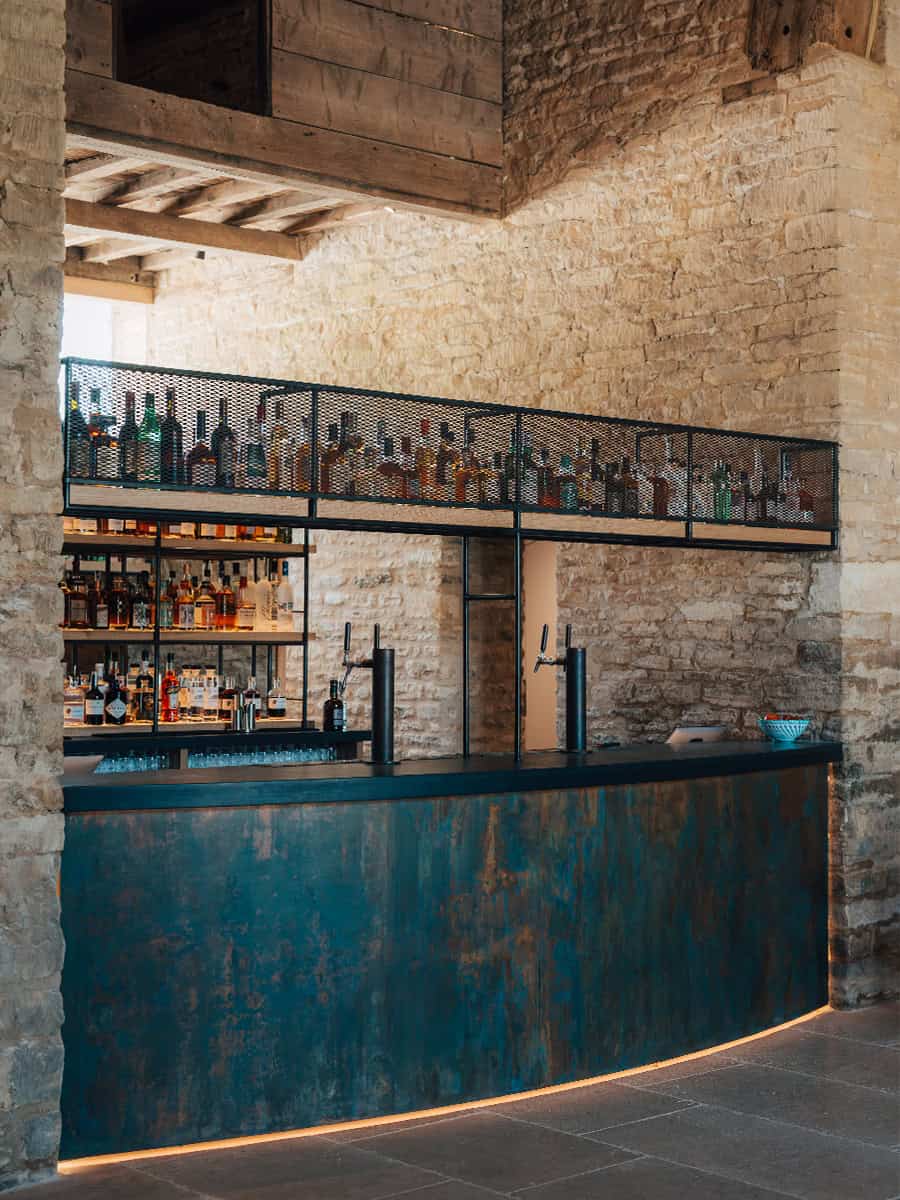 Ivy Lodge patinated copper bar with spirit shelves against original Cotswolds stonework, heritage restoration